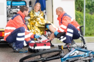 An injured cyclist receiving medical treatment from two paramedics before calling a bicycle accident attorney in Birmingham.