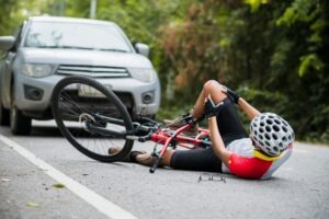 An injured cyclist lying in the road in front of a car before calling a bicycle accident attorney in Montgomery.