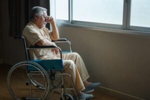 A sad man in a wheelchair contemplates calling a nursing home abuse and neglect lawyer.